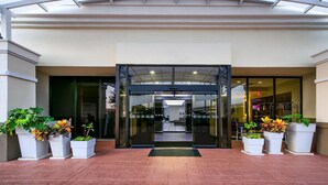 A hotel entrance with a glass door, potted plants, and a tiled floor. - Wyndham Houston Sugarland (Houston)