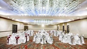 A banquet hall with round tables, white tablecloths, and chairs with red sashes. - Wyndham Houston Sugarland (Houston)