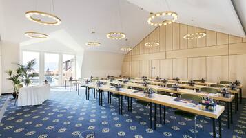 A conference room with multiple tables and chairs, a patterned carpet, and a ceiling with circular light fixtures.