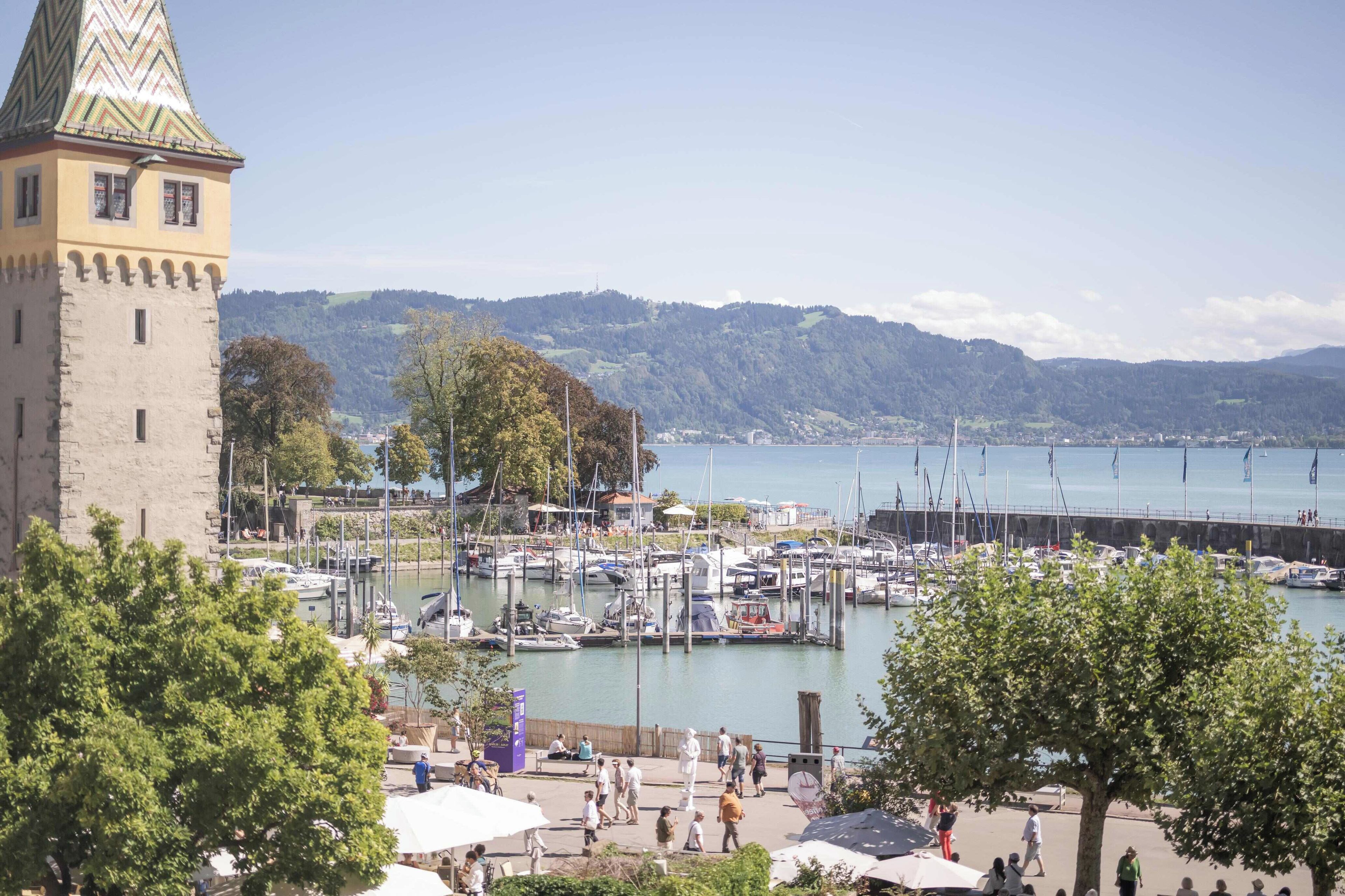 Ein Yachthafen mit vertäuten Booten, ein Turm und eine hügelige Landschaft im Hintergrund.