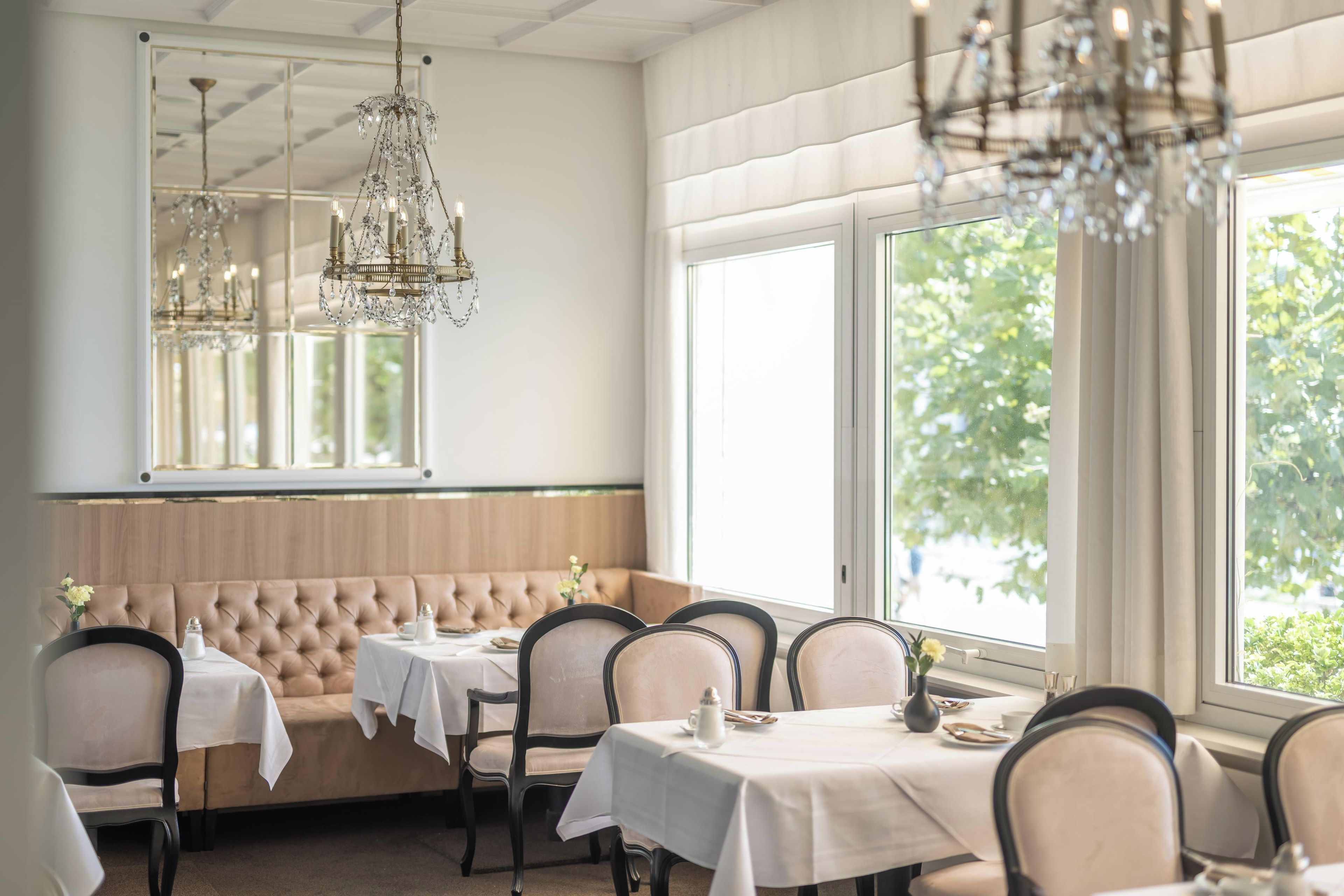 A dining area with a booth seating arrangement, tables with white tablecloths, and a chandelier.