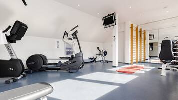 Een moderne sportschool met cardioapparatuur, krachtapparaten en een televisiescherm.