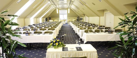 A conference room with rows of tables, chairs, and a stage at the front.