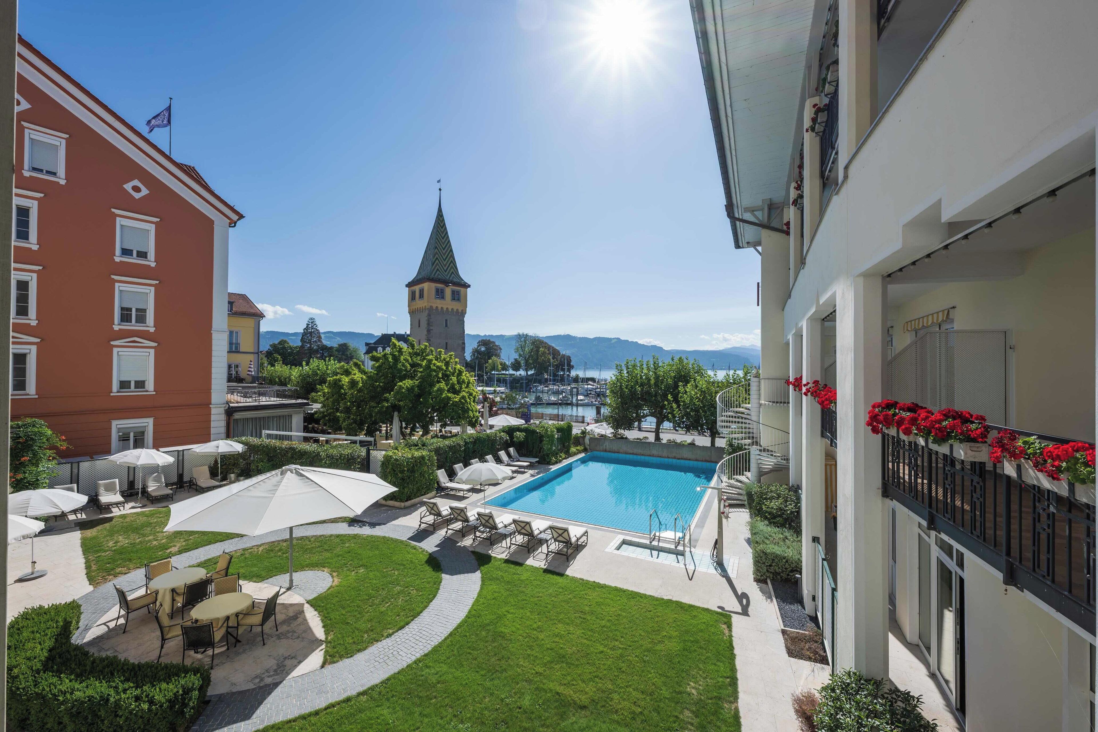 Un patio de hotel con piscina, sillas de descanso y vistas a una torre y montañas.