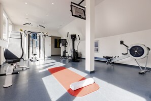 Un gimnasio con diverso equipo de ejercicio, una colchoneta roja y una toalla blanca.
