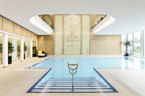 Una piscina interior moderna con una fuente central, rodeada de paneles de madera y ventanas amplias.