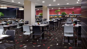 Un restaurante espacioso con varias mesas y sillas, un suelo con estampado y una pared de acento roja decorada con plantas.