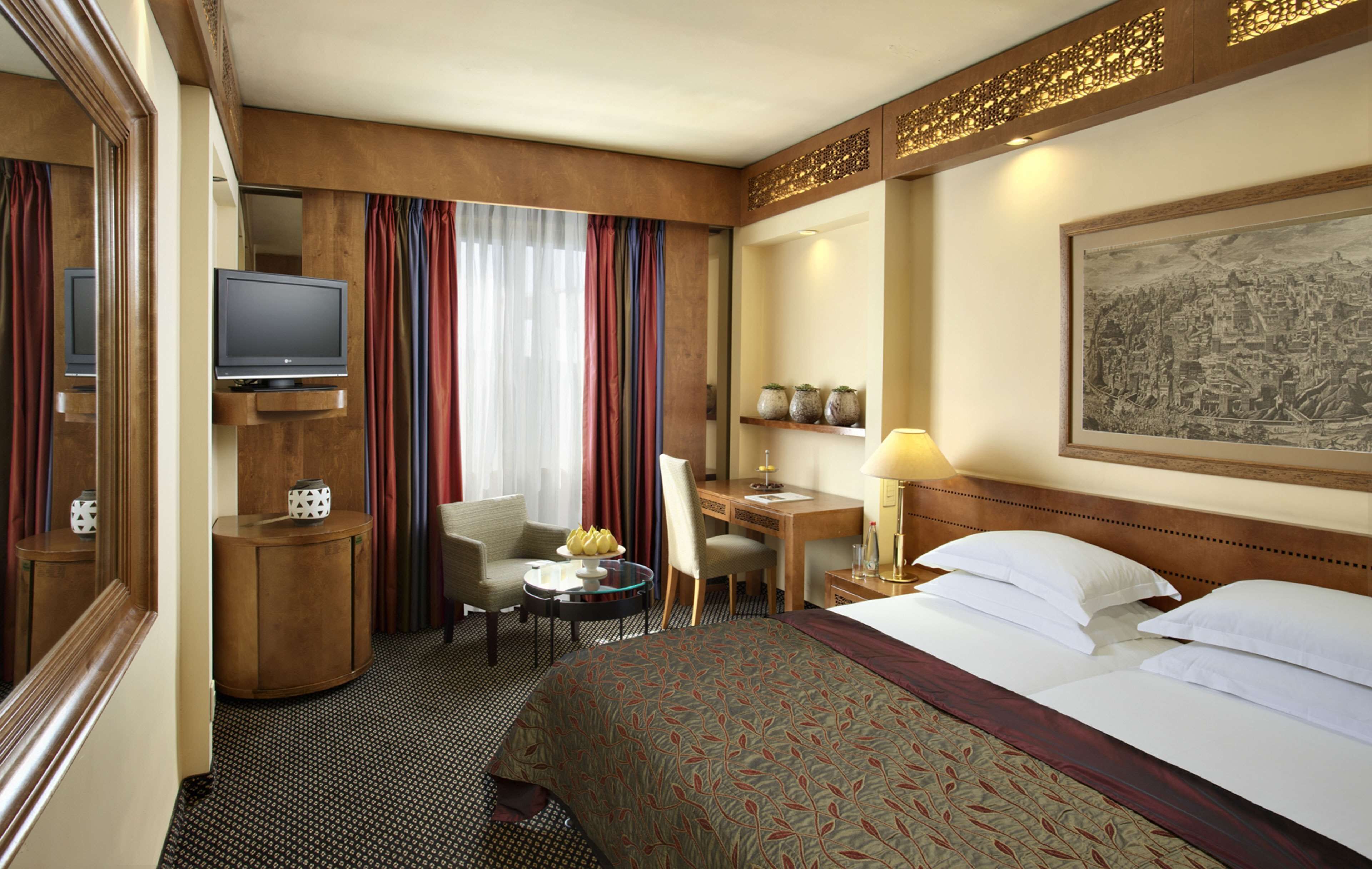 A hotel room with a bed, desk, chair, television, and a painting on the wall.