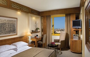 A hotel room with a bed, desk, chair, TV, and a view of the city.