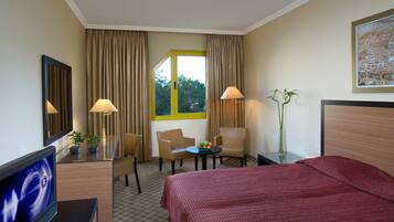Habitación de hotel con cama, dos sillas, una mesita con fruta, televisor y ventana con cortinas.