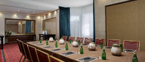 A conference room with a long table, red chairs, and green bottles.