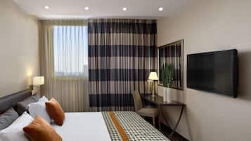 A hotel room with a bed, a desk, a chair, a TV, and a window with curtains.