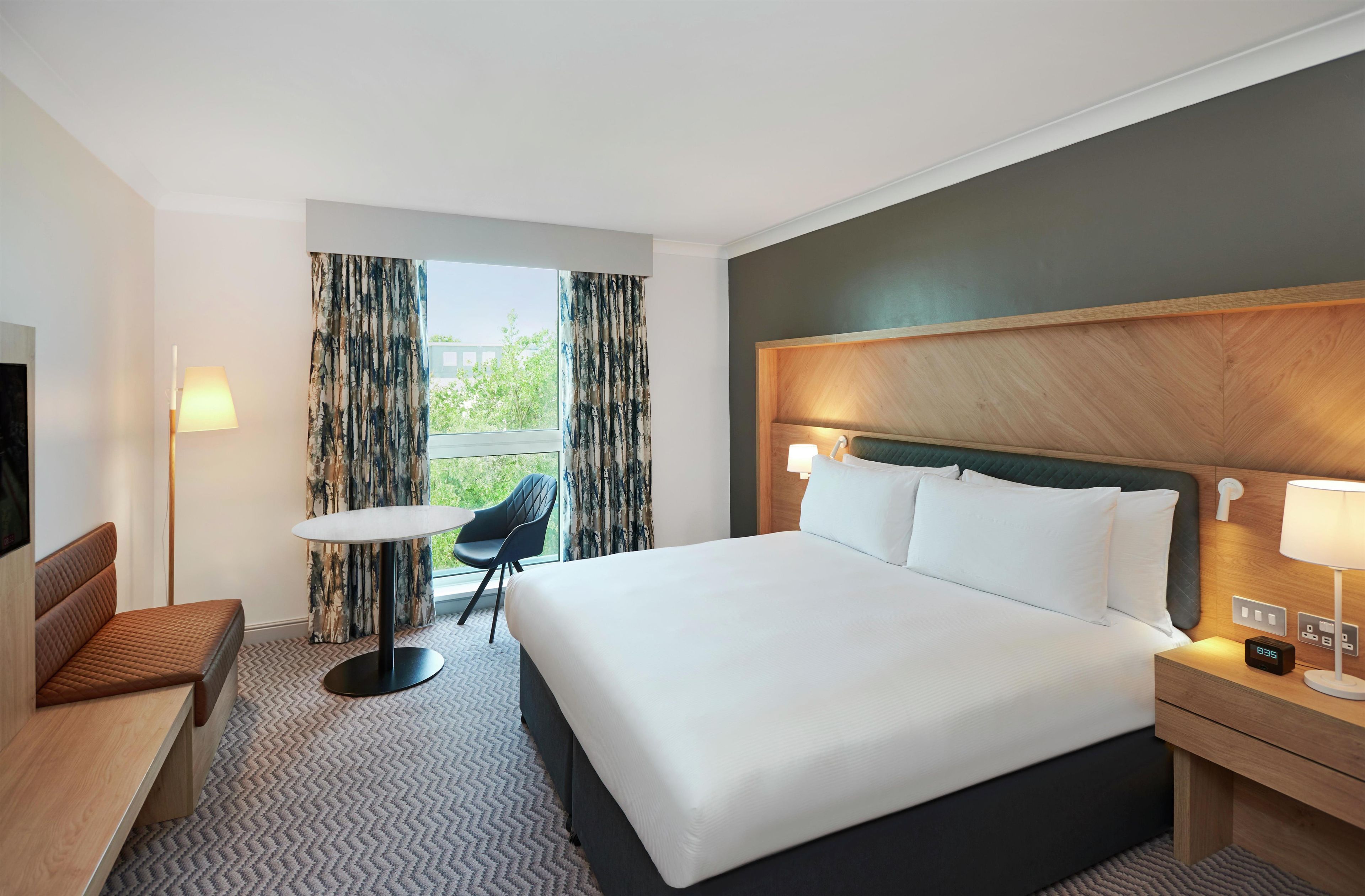 Een hotelkamer met een bed, nachtkastje, lamp, stoel en een televisie.