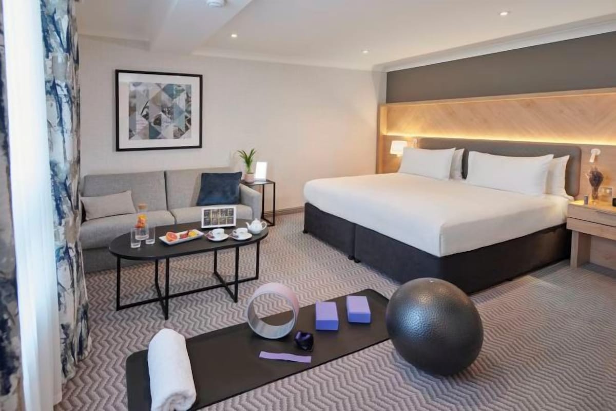 A hotel room with a bed, a sofa, a coffee table, and a small table with a lamp.