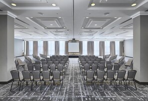 A conference room with rows of chairs, a large screen, and a carpeted floor.