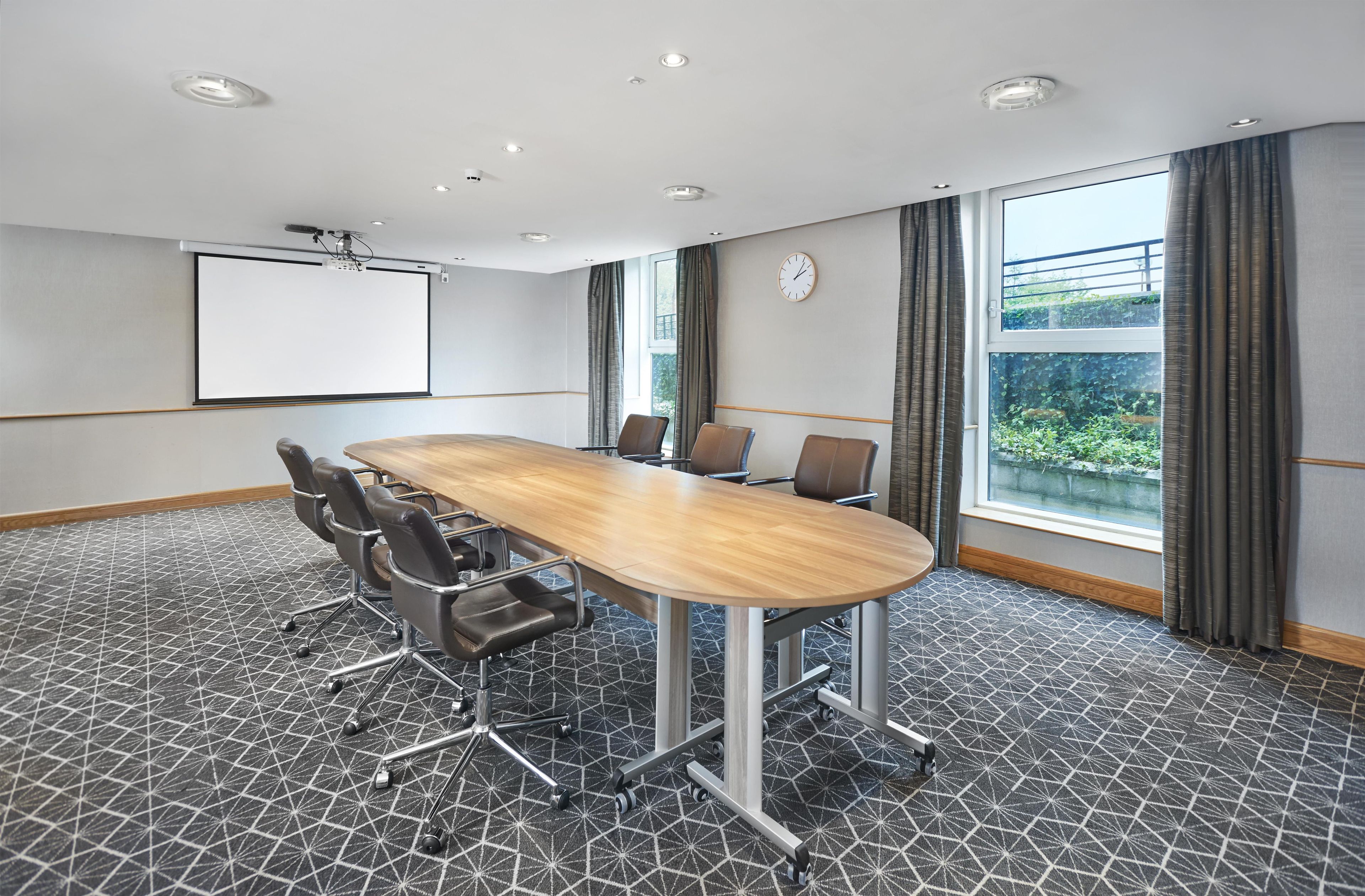A conference room with a large table, chairs, a projector screen, and a clock on the wall.