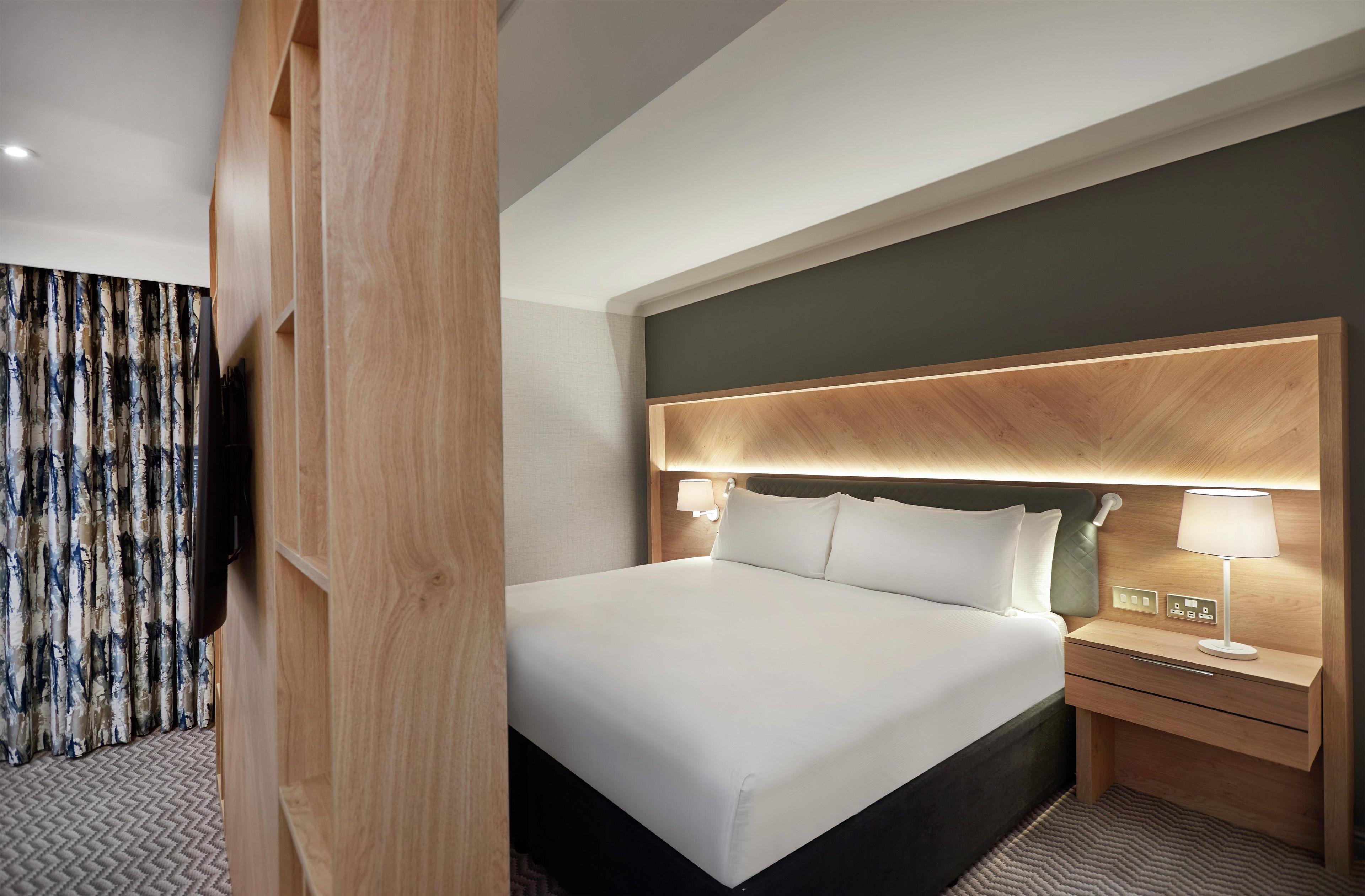 A hotel room with a large bed, bedside tables, and a headboard with integrated lighting.