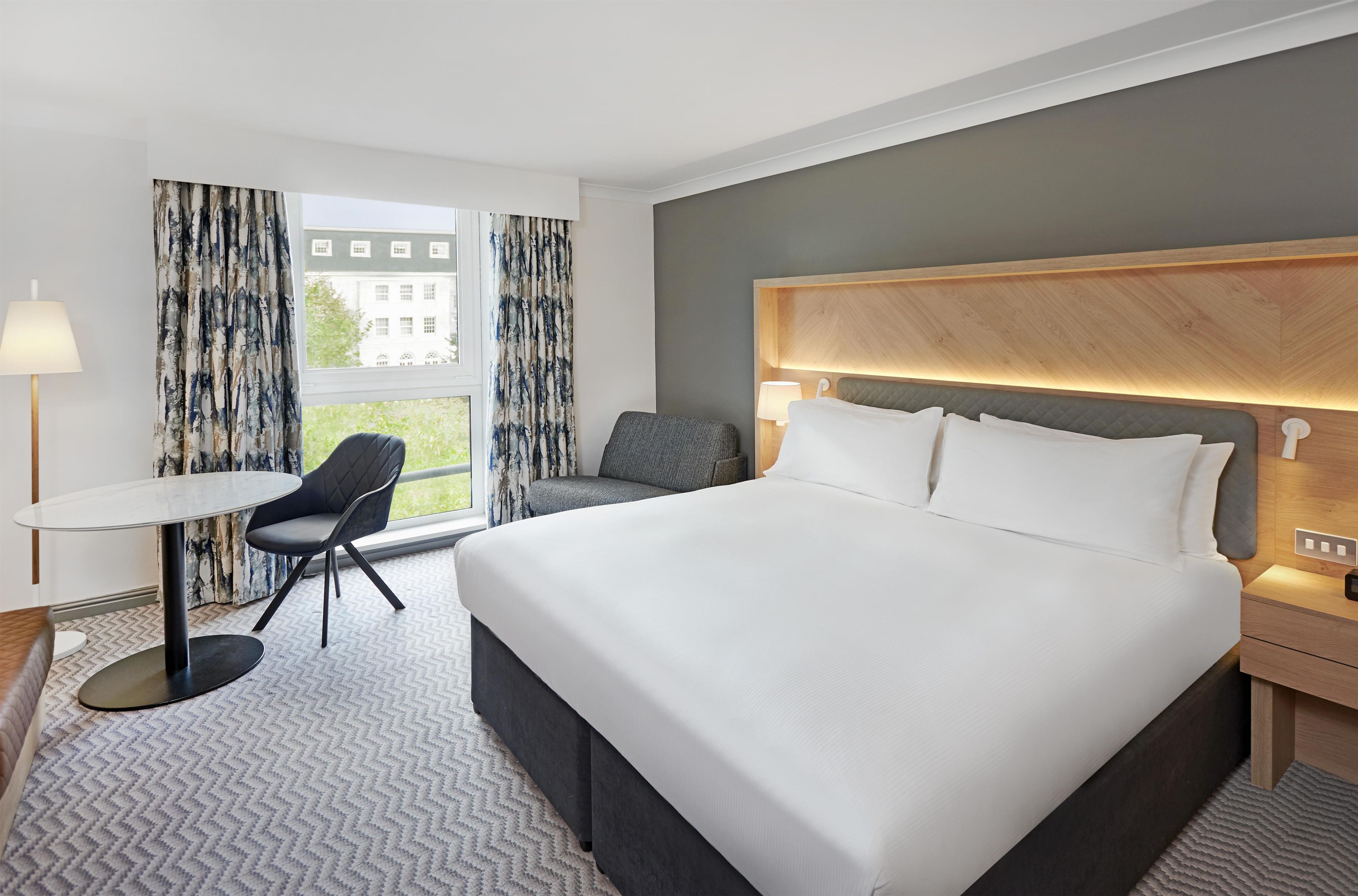 A hotel room with a large bed, a desk, a chair, and a view of the outside.