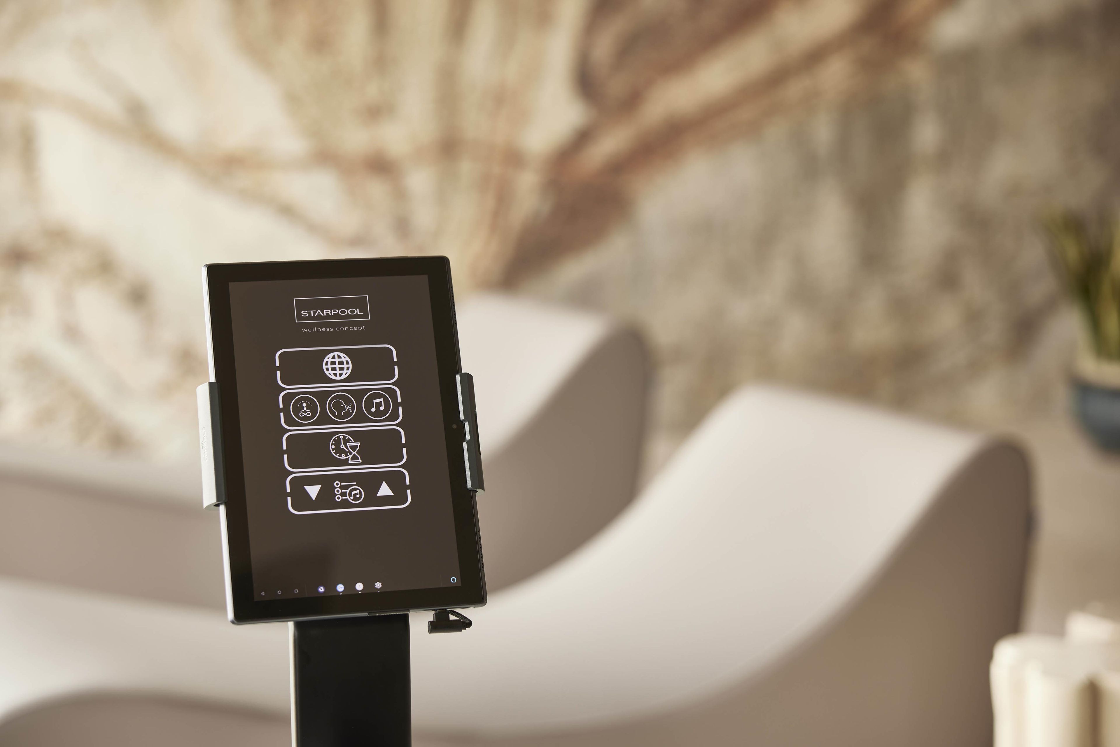 A digital kiosk with wellness concept icons, positioned in front of a modern sofa and a textured wall.