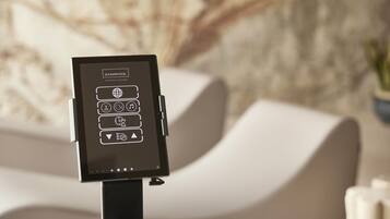 A digital kiosk with wellness concept icons, positioned in front of a modern sofa and a textured wall.