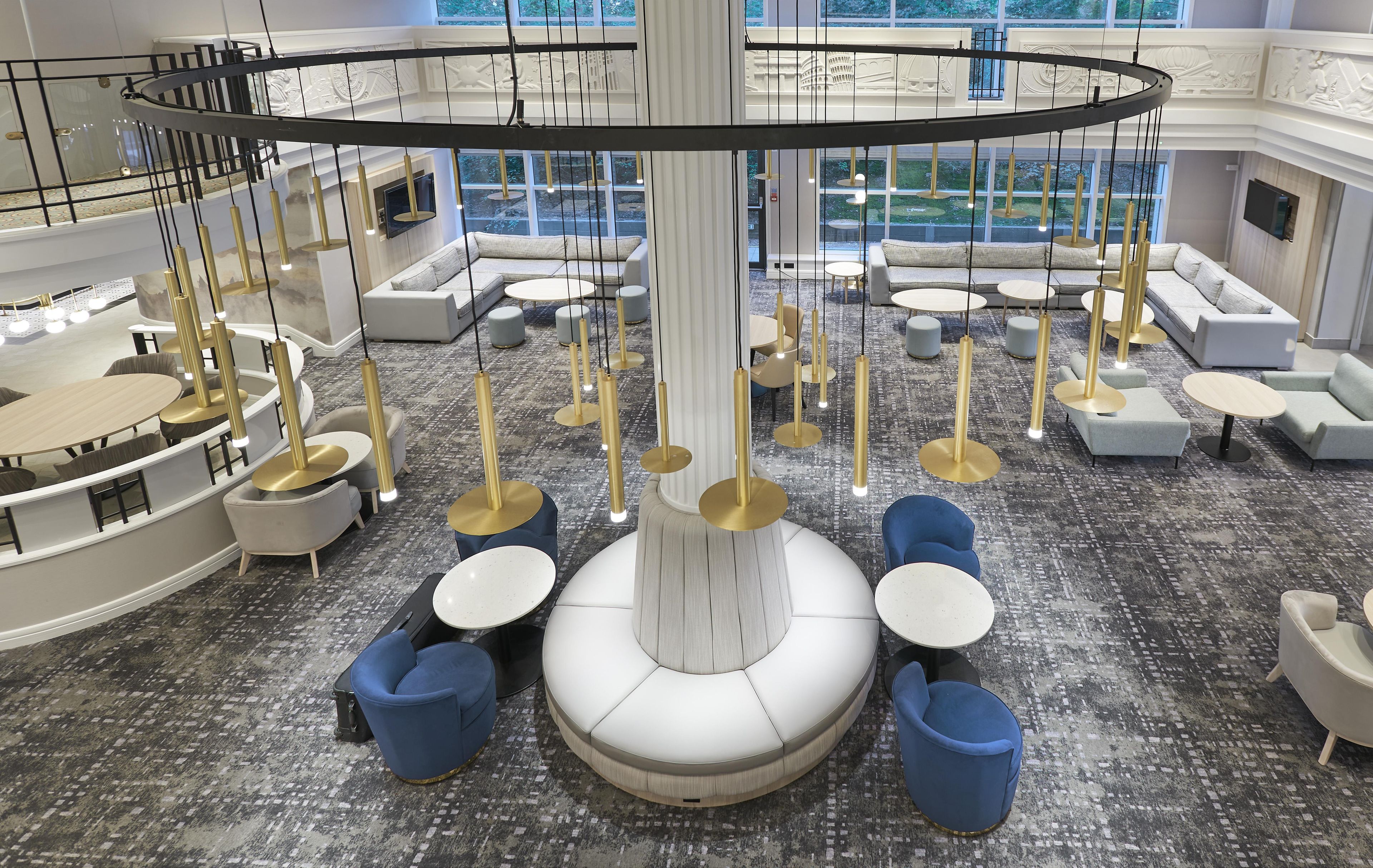 Ampla área de estar com diversas opções de assento, incluindo sofás e mesas redondas, e um colunar decorativo central.