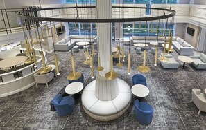 A spacious lounge area with multiple seating options, including sofas and round tables, and a central decorative column.