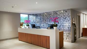A hotel reception desk with a digital check-in station, a large window, and a wall with a geometric pattern.