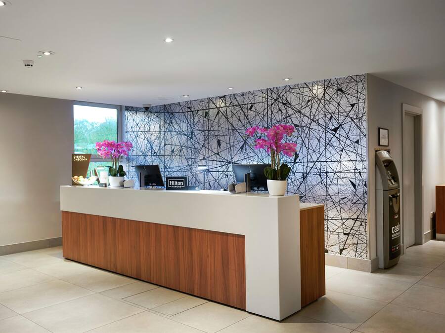 A hotel reception desk with a digital check-in station, a large window, and a wall with a geometric pattern.