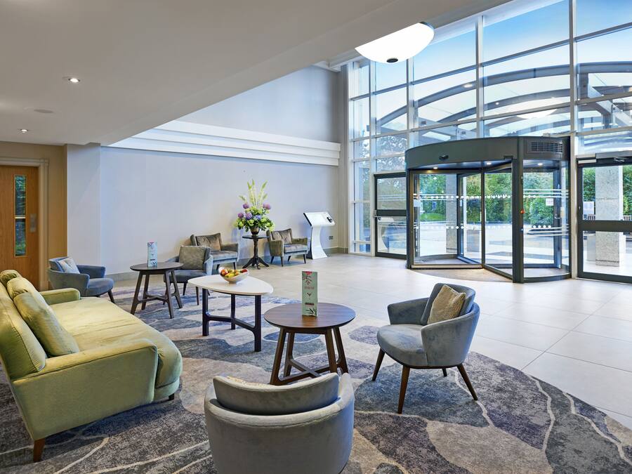 A spacious lobby with a green sofa, armchairs, a small table with a vase, and a revolving door.