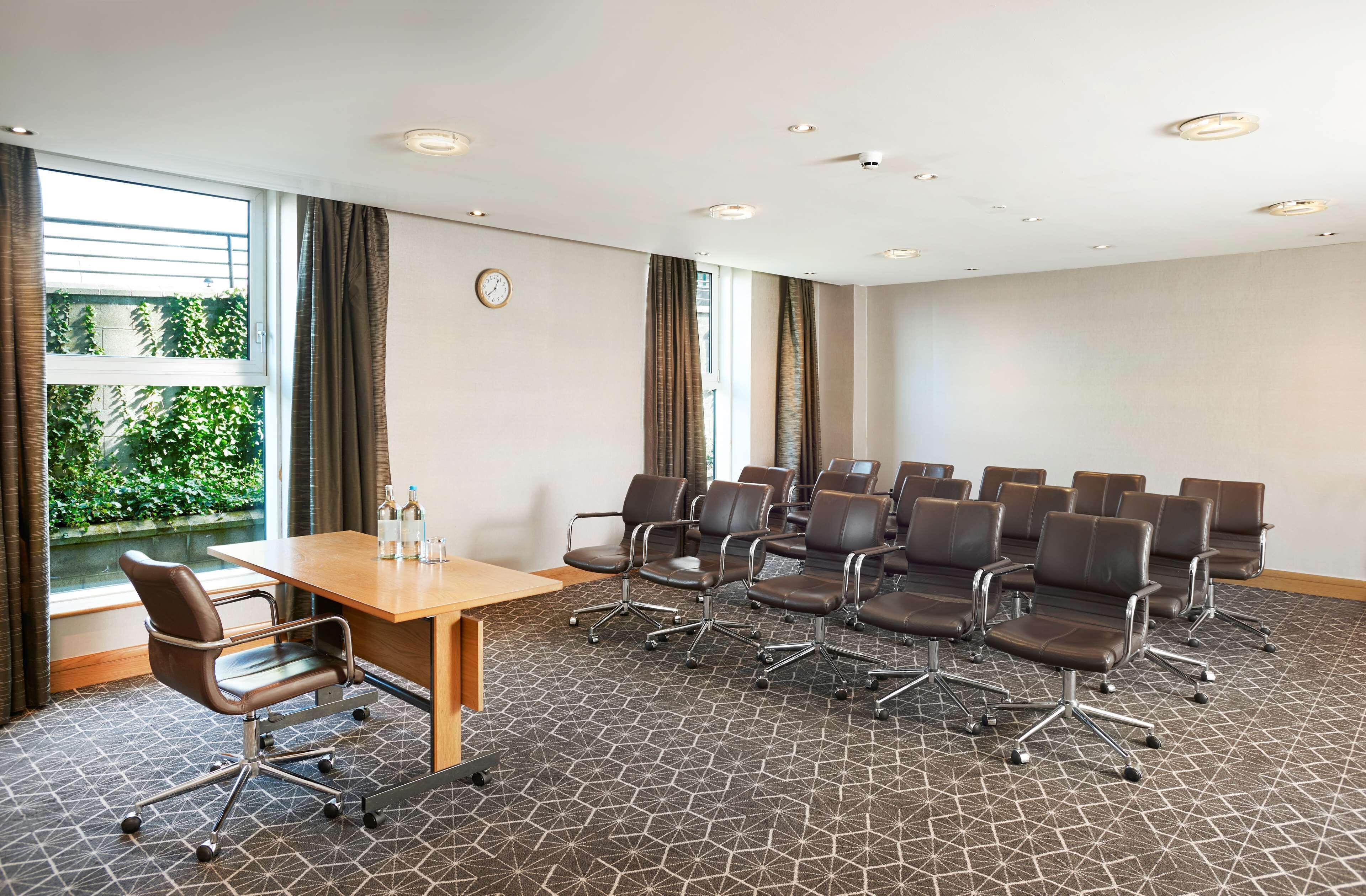 A conference room with a wooden table, multiple chairs, and a clock on the wall.