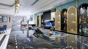 A bar area with a marble countertop, bar stools, a cash register, and shelves with liquor bottles.