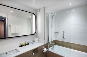 A modern bathroom with a large mirror, a bathtub, a shower, and a vanity with toiletries. - Hilton London Croydon (Croydon)