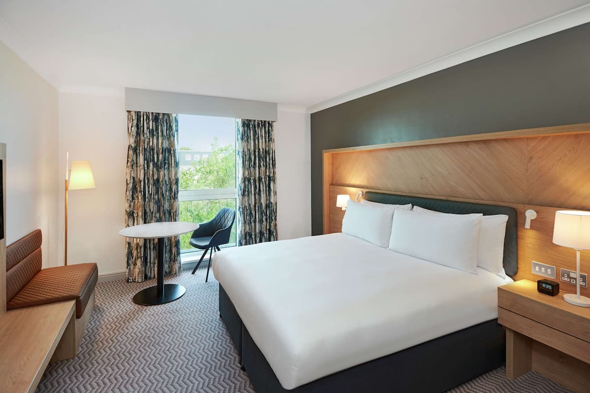 Habitación de hotel con una cama grande, un escritorio, una silla, una mesita y un televisor.