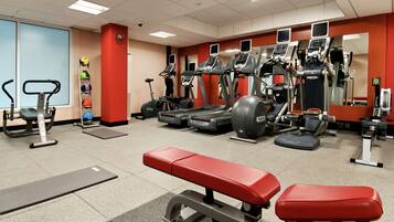 Un gimnasio con cintas de correr, elípticas, una banca y una bicicleta estática de pared.