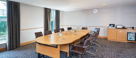 A conference room with a long table, chairs, a clock, and a minibar.