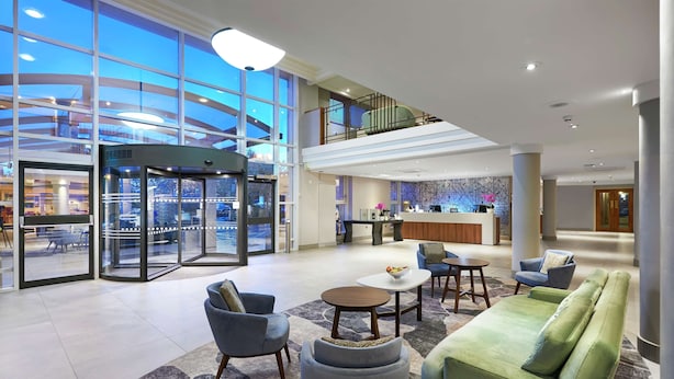 A spacious lobby with a central seating area, a reception desk, and a glass elevator.