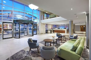 A spacious lobby with a central seating area, a reception desk, and a glass elevator. - Hilton London Croydon (Croydon)