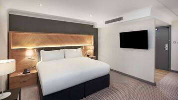 A modern hotel room with a large bed, bedside tables, a flat-screen TV, and a wooden headboard.