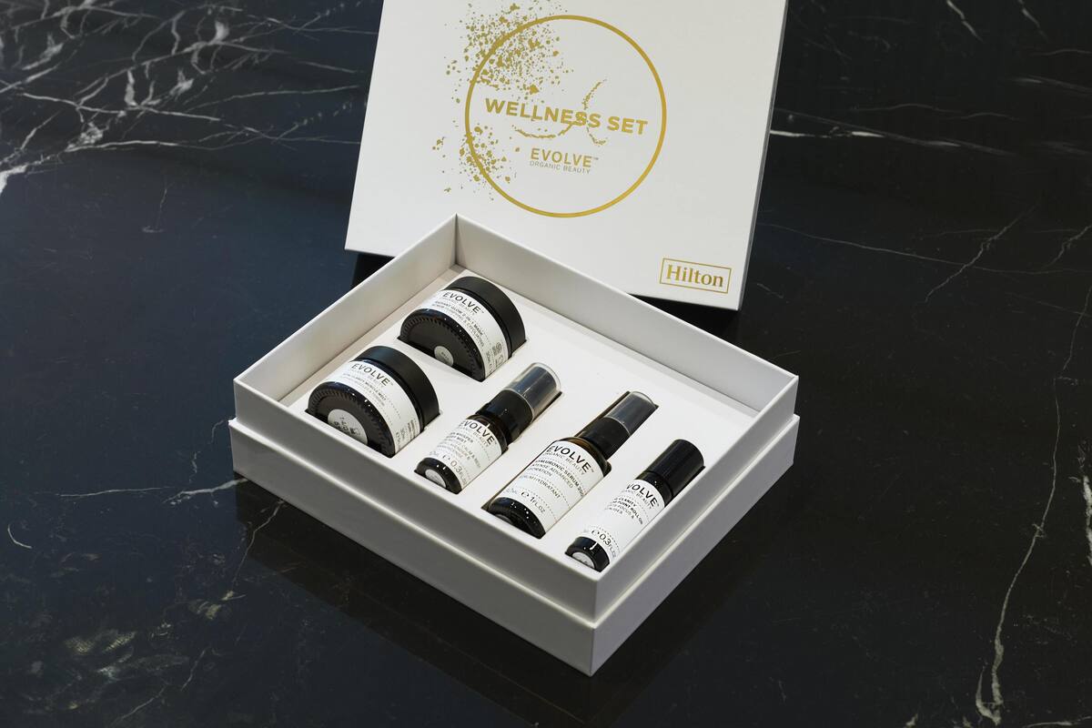 Una caja blanca con un logotipo dorado y texto, que contiene cuatro botellas negras y otra caja blanca con texto.