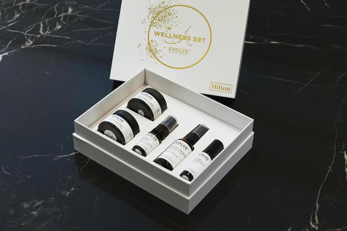 Eine weiße Schachtel mit dem Aufdruck 'Wellness Set' und 'Hilton'-Branding, gefüllt mit vier schwarz-weißen Flaschen.