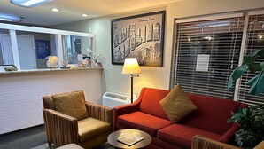 A hotel lobby with striped armchairs, a red sofa, a small table with a book, a lamp, and a framed welcome sign.
