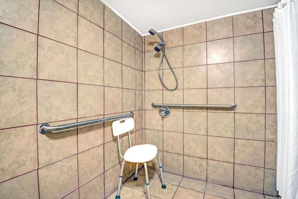 Un baño con ducha, barra de apoyo y asiento accesible para sillas de ruedas.