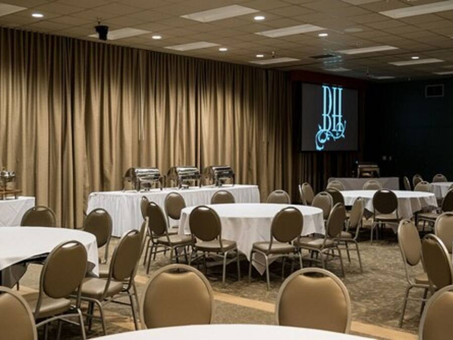 A conference room with round tables and chairs, a large screen displaying "BHI" in the background, and a curtain wall.