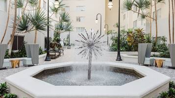 A courtyard with a central fountain, surrounded by seating areas and palm trees.
