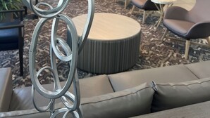 A modern lounge area with sofas, armchairs, and a decorative metal sculpture. - Brent House Hotel (New Orleans)