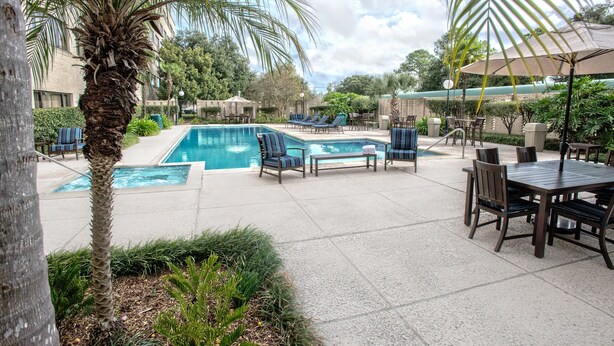 A pool area with lounge chairs and umbrellas, surrounded by palm trees and greenery. - Brent House Hotel (New Orleans)
