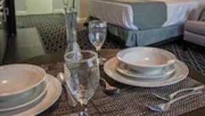 A hotel room with a neatly arranged dining table, a vase with flowers, and a bed with a blue headboard. - Brent House Hotel (New Orleans)
