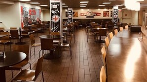 A spacious restaurant with high ceilings, multiple seating areas, and a central column with a logo. - Brent House Hotel (New Orleans)