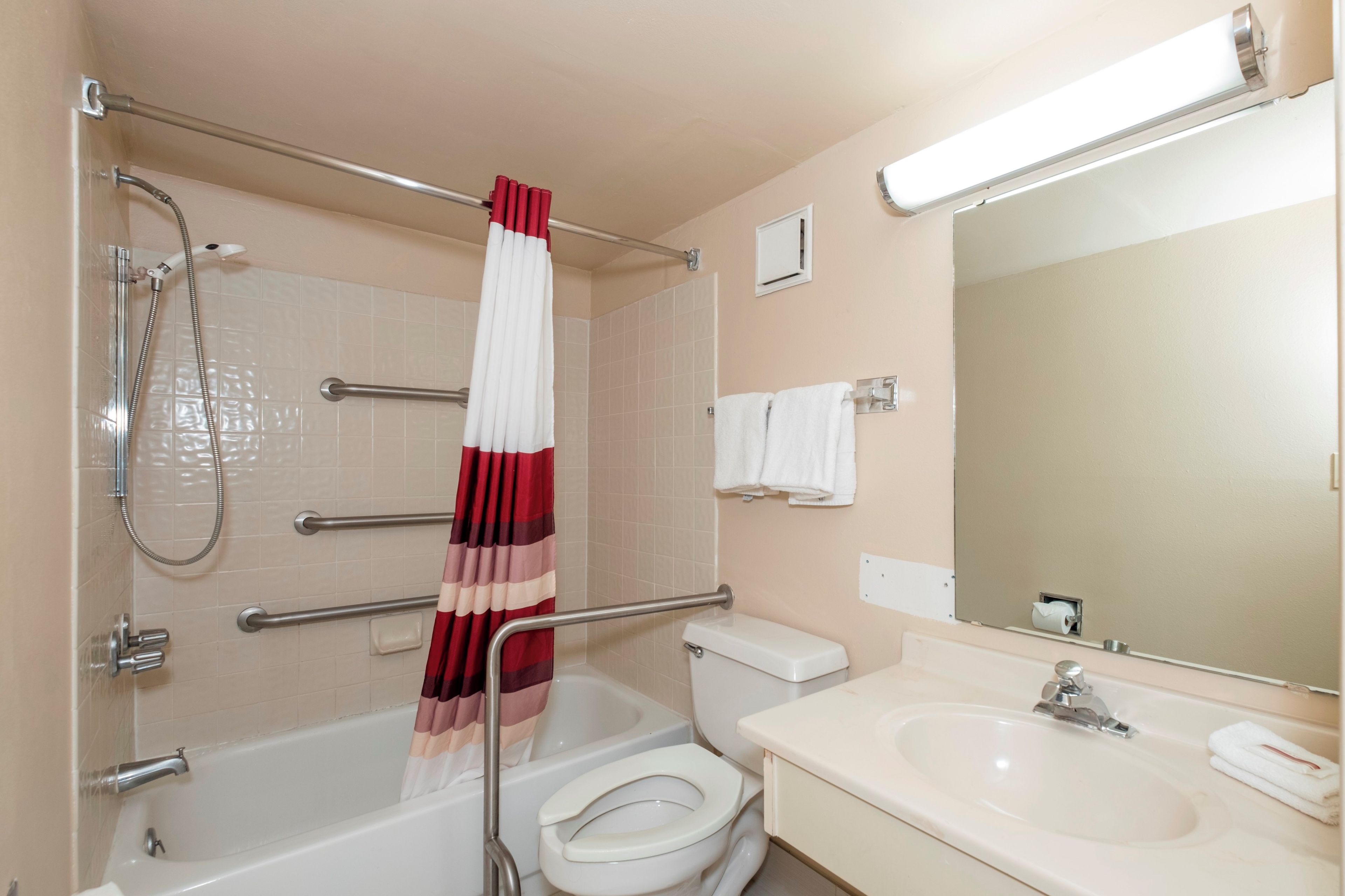 A bathroom with a bathtub, toilet, and sink, equipped with grab bars and a shower head.