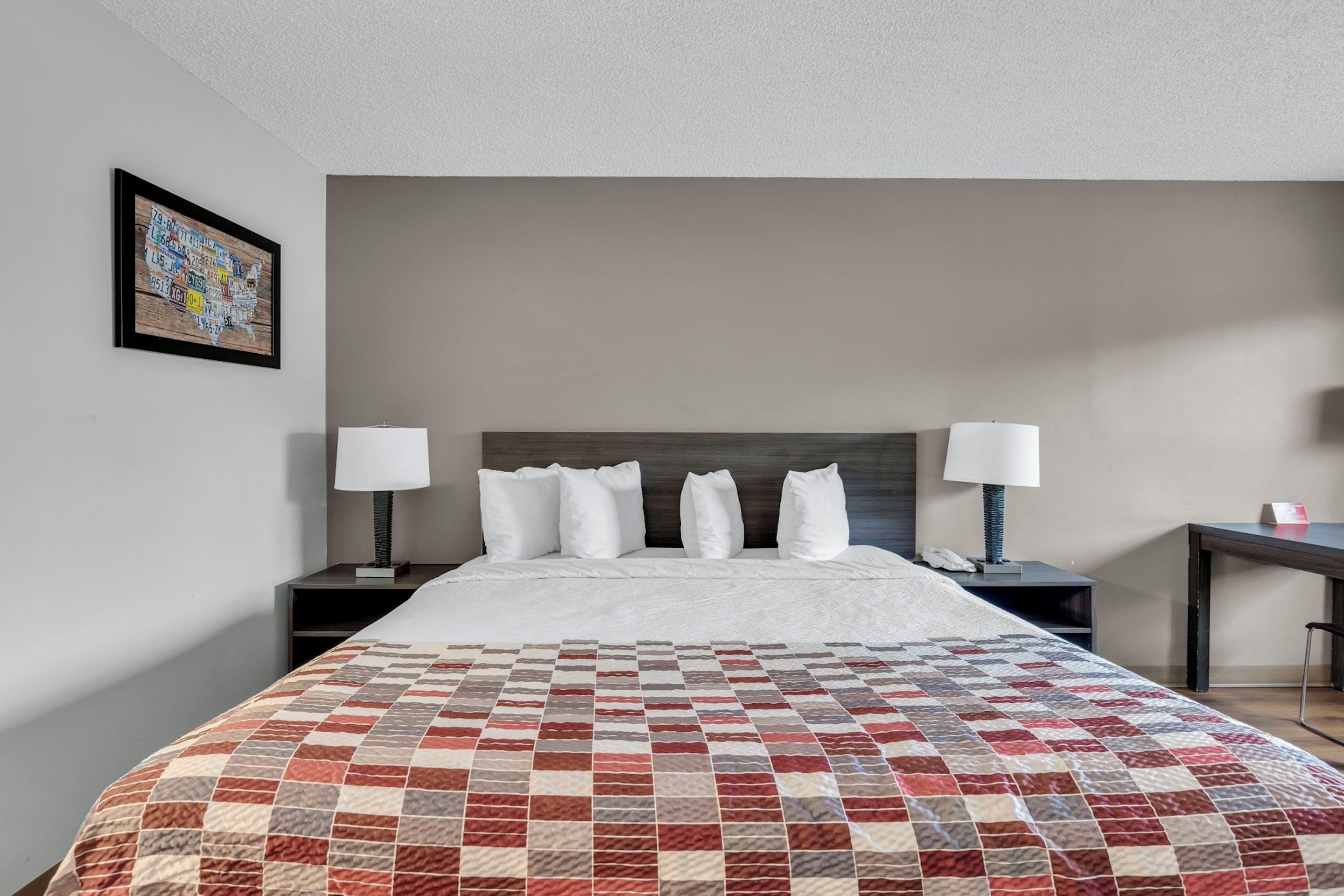 A hotel room with a bed, two bedside tables with lamps, a nightstand, and a framed picture on the wall.